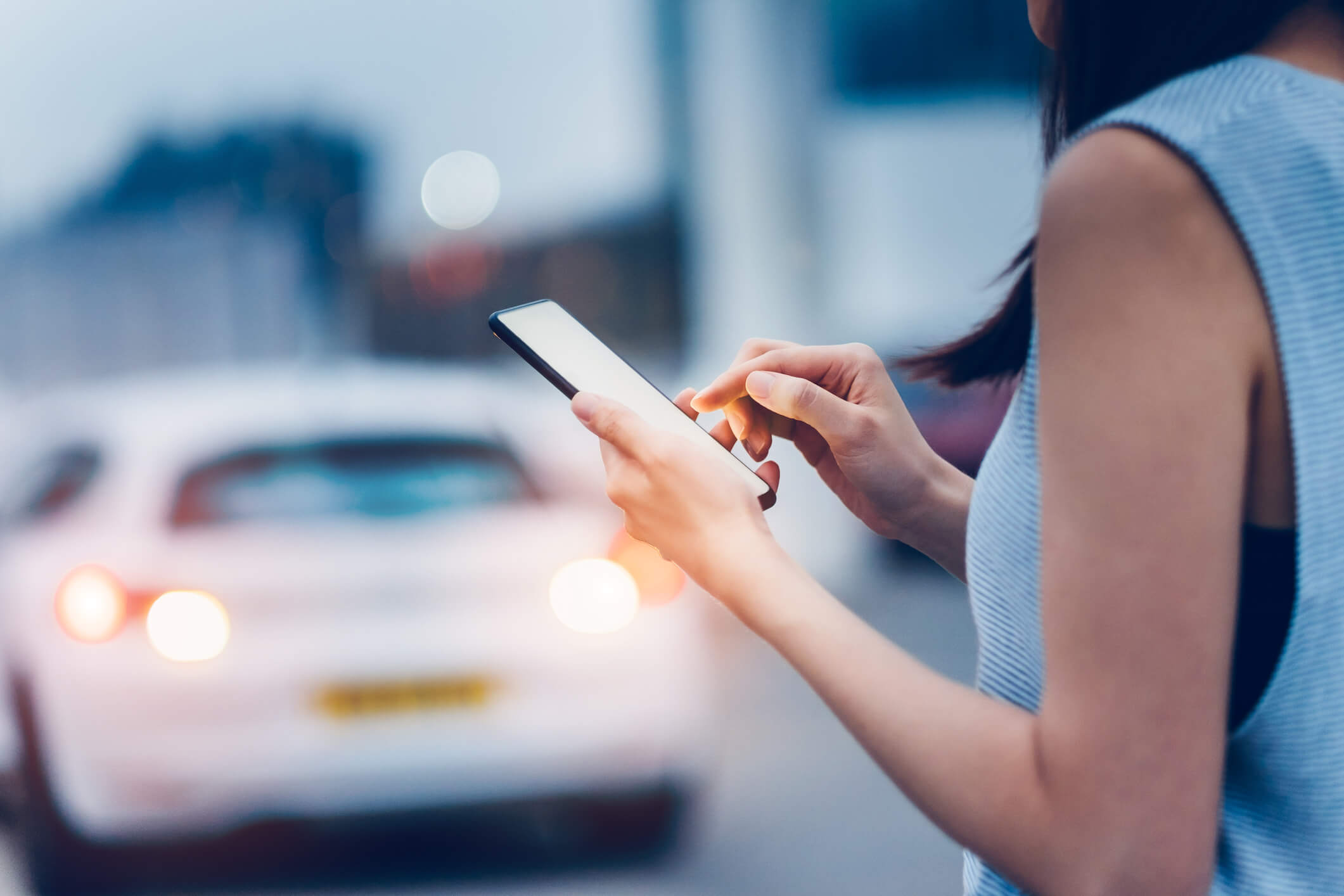 Woman using smartphone while waiting for a taxi ride on city street