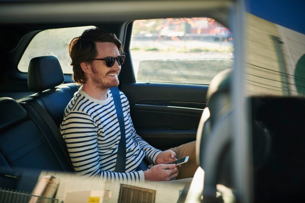 Smiling man with mobile phone sitting in backseat of car